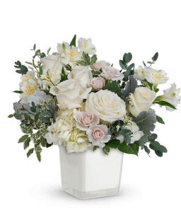 A serene arrangement featuring white hydrangea, white roses, white spray roses, white alstroemeria, white limonium, and floral greens, all elegantly presented in a white cube. This all-white display offers a timeless and peaceful touch to any occasion.